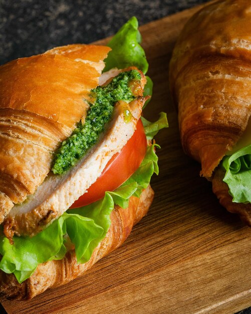 Photo un sandwich au pesto de poulet frais avec de la laitue et de la tomate sur une planche à couper en bois