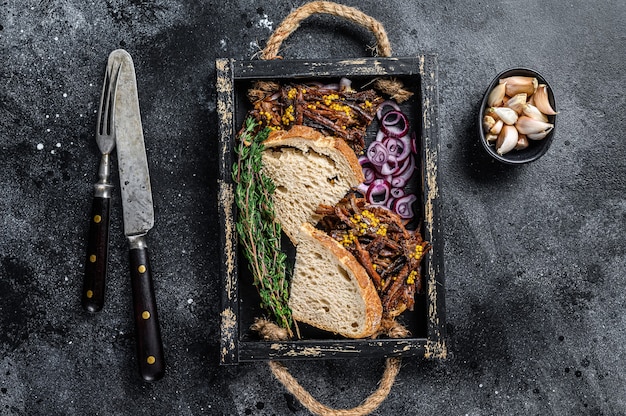 Sandwich au porc effiloché avec viande de porc fumée dans un plateau en bois. Fond noir. Vue de dessus.