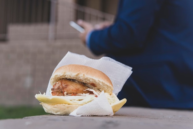 Sandwich au poulet allongé sur un banc dans la rue concept de malbouffe pendant la pause déjeuner L'homme d'affaires mange des aliments riches en calories malsains dans la rue dans le contexte d'un immeuble de bureaux