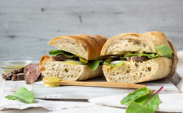 Sandwich au rôti de boeuf avec salade, oignons et cukes et sauce à la moutarde.