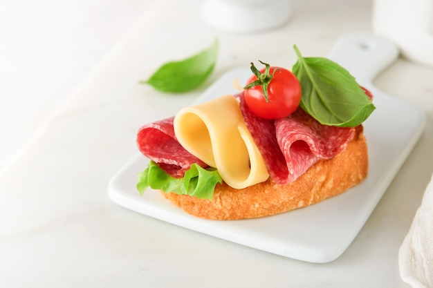 Sandwich au salami Des sandwichs grillés délicieux avec des tranches de salami, du fromage cheddar, de la laitue et des tomates, des cerises sur un fond de marbre blanc.