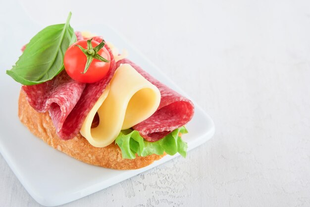 Sandwich au salami Des sandwichs grillés délicieux avec des tranches de salami, du fromage cheddar, de la laitue et des tomates, des cerises sur un fond de marbre blanc.