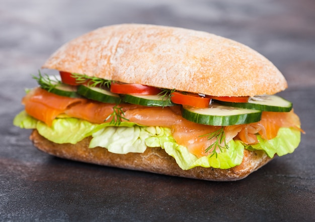 Sandwich au saumon frais et sain avec laitue et concombre sur fond de pierre noire. Collation du petit déjeuner