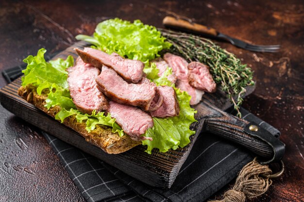 Sandwich au steak avec rosbif tranché, salade et légumes. Fond sombre. Vue de dessus.