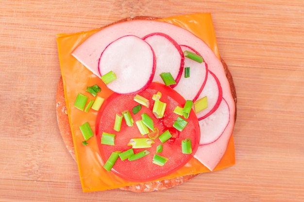 Photo sandwich aux craquelins croustillants avec fromage, saucisses aux tomates, oignons verts et radis