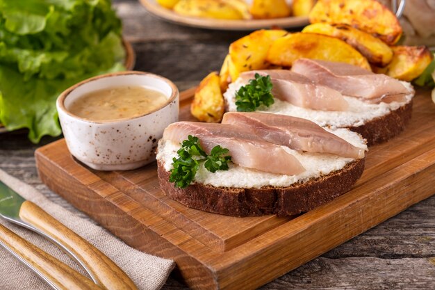 Sandwich Aux Filets De Hareng Et Pomme De Terre Au Four Sur Une Planche De Bois.