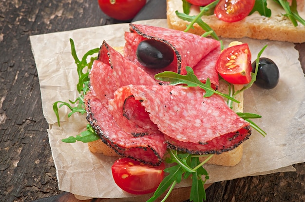 Sandwich aux saucisses, olive, tomate et roquette sur l'ancienne table en bois