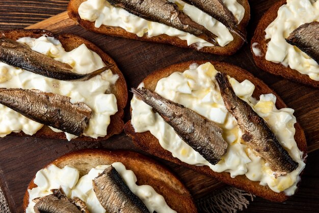 Sandwich aux sprats, œufs et mayonnaise sur table en bois.