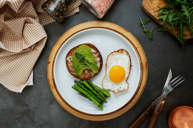 Sandwich à l'avocat grillé et un œuf au plat sur une plaque blanche aux asperges. Nourriture saine ou petit déjeuner.