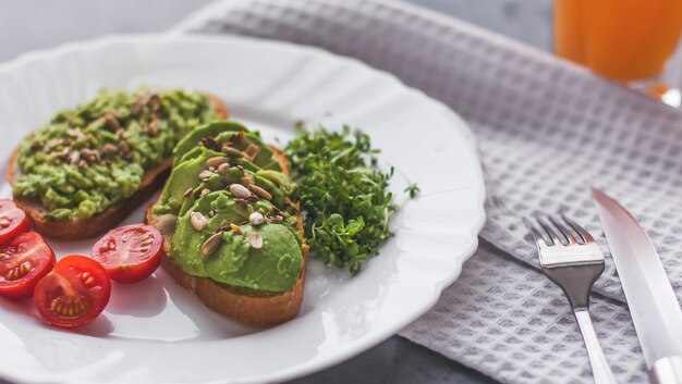 Sandwich à l'avocat végétalien avec tomates et micropousses sur une plaque blanche sur une surface grise