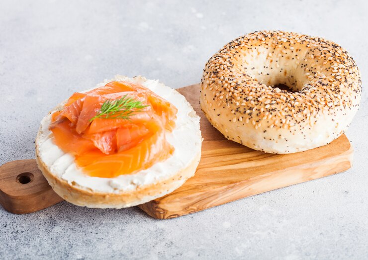 Photo sandwich bagel frais et sain avec du saumon, de la ricotta et de l'aneth sur une planche à découper vintage sur une table de cuisine légère.