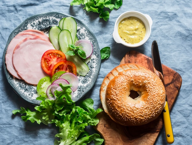 Sandwich bagel avec légumes au jambon et salade verte sur fond bleu vue de dessus