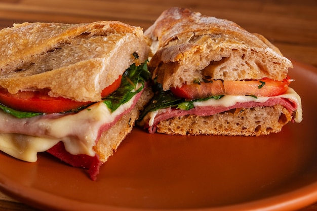 sandwich à la baguette artisanale avec de la mozzarella fondue, de la mortadella, de l'arugula et des tranches de tomate