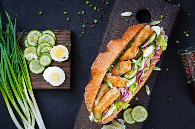 Sandwich baguette avec poisson, œuf, oignons marinés et feuilles de laitue. Vue de dessus