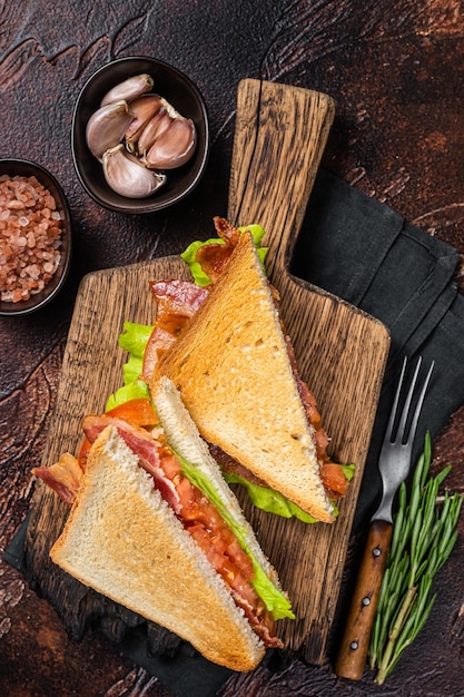 Sandwich BLT classique avec bacon, tomate et laitue sur planche de bois avec herbes Fond sombre Vue de dessus