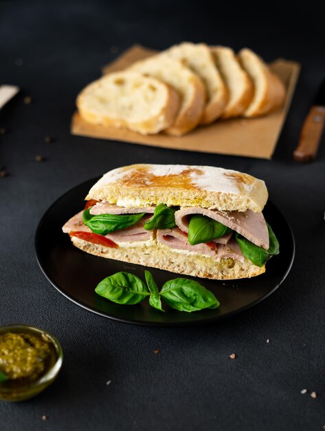 Sandwich Ciabatta au Jambon Sauce Pesto Tomates Basilic sur fond noir Nourriture Nourriture backgroun