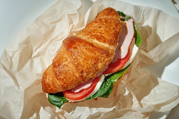 Photo un sandwich croissant au jambon, épinards et tomate nappe blanche légère dure