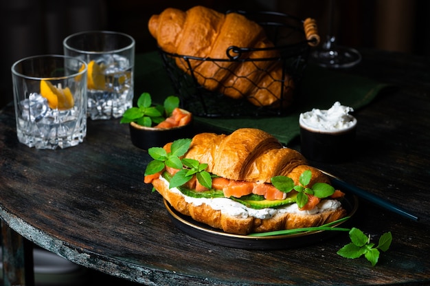 Sandwich croissant au saumon salé sur plaque noire, servi avec des feuilles de basilic frais, de l'avocat et du fromage Philadelphia. Petit déjeuner français. Concept d'alimentation saine.