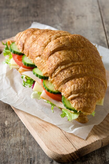 Sandwich croissant avec du fromage, du jambon et des légumes sur une table en bois