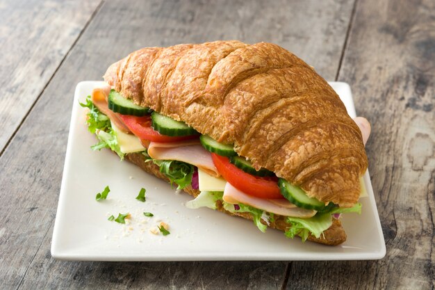 Sandwich croissant avec du fromage, du jambon et des légumes sur une table en bois