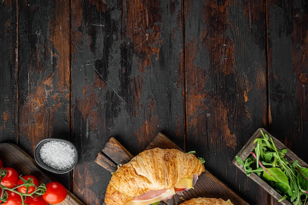 Sandwich croissant frais avec du jambon, du fromage et de la feuille de salade, avec des herbes et des ingrédients, sur le vieux fond de table en bois sombre, vue de dessus à plat, avec copie espace pour le texte