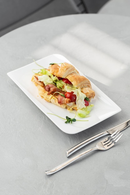 Sandwich croissant avec tomates bacon et salade de laitue sur plaque blanche et fond clair