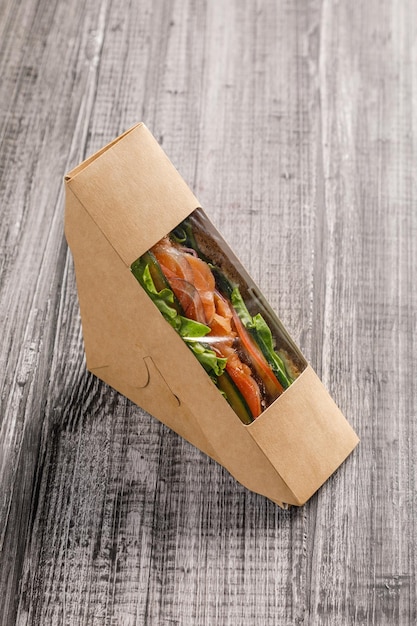 Photo sandwich dans un récipient à emporter sur fond de bois gris