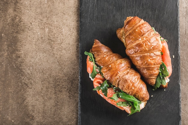 Sandwich deux croissants au saumon, ricotta et roquette sur une ardoise noire