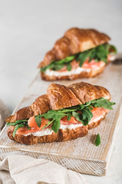 Sandwich à deux croissants au saumon, ricotta et roquette sur une planche de bois avec une serviette