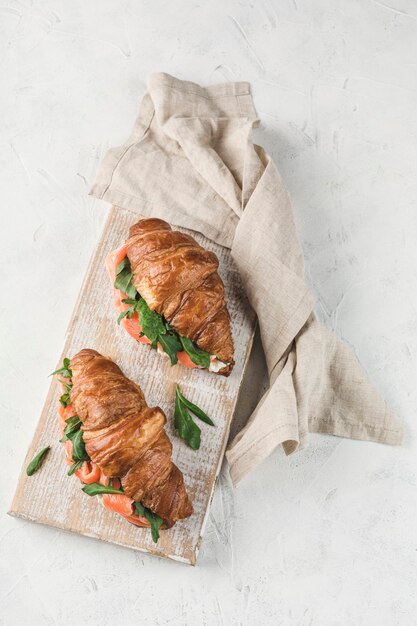 Sandwich à deux croissants au saumon, ricotta et roquette sur une planche de bois avec une serviette