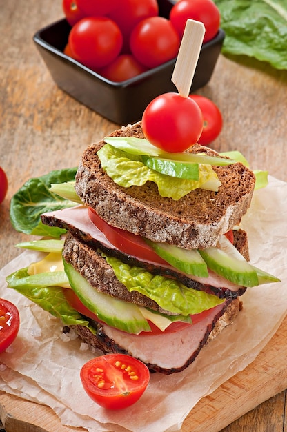 Sandwich avec du jambon et des légumes frais sur un fond en bois