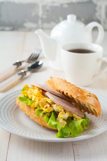 Sandwich farci aux œufs brouillés, au jambon et aux feuilles de laitue sur un fond en bois clair. Mise au point sélective.