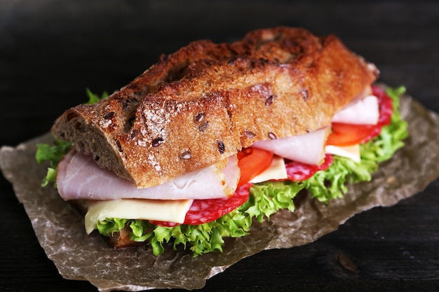 Photo sandwich frais et savoureux avec du jambon et des légumes sur papier sur fond de bois