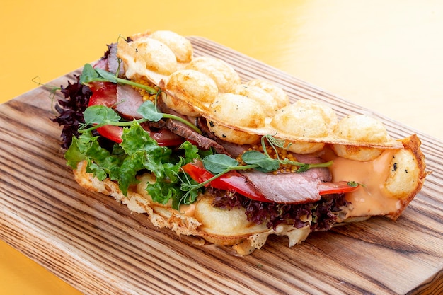 Sandwich à la gaufre à bulles avec jambon, tomate et laitue Sur une planche de bois