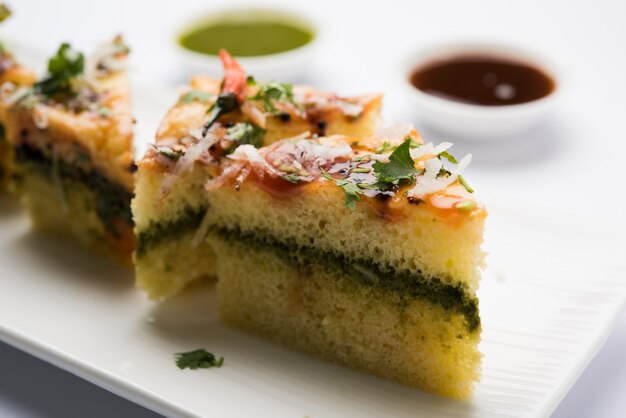 Le sandwich jaune Dhokla est un en-cas salé indien à base de farine de pois chiches ou de farine de riz, originaire du Gujarat. Servi avec chutney vert et tamarin. mise au point sélective