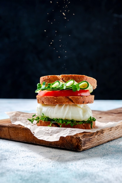 Sandwich maison sain avec du pain de grains entiers, œuf poché, concombre, tomate et micro-herbes Salade de cresson sur planche de bois.