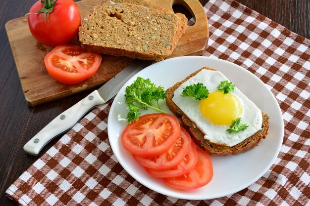 sandwich avec œuf au plat sur la plaque blanche avec tomates et pain de grains entiers