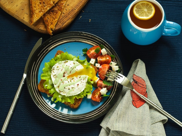 Sandwich, œuf poché et salade sur fond sombre