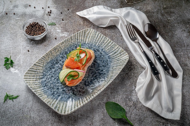 Sandwich ouvert au saumon, bar, concombre et radis sur une table en pierre grise