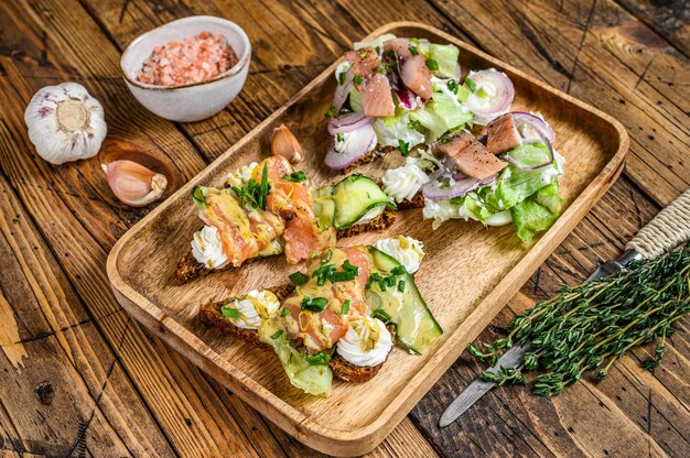 Sandwich ouvert au saumon et hareng, fromage à la crème et salade sur une planche à découper