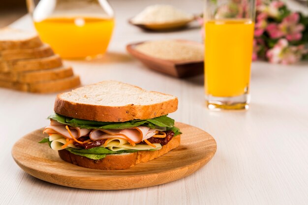 Sandwich sur une plaque blanche avec poitrine de dinde, tomate, laitue et fromage sur la table