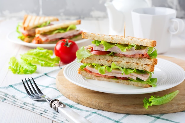 Sandwich pour le petit déjeuner avec tomates farcies au jambon et laitue sur une surface en bois clair. Mise au point sélective.