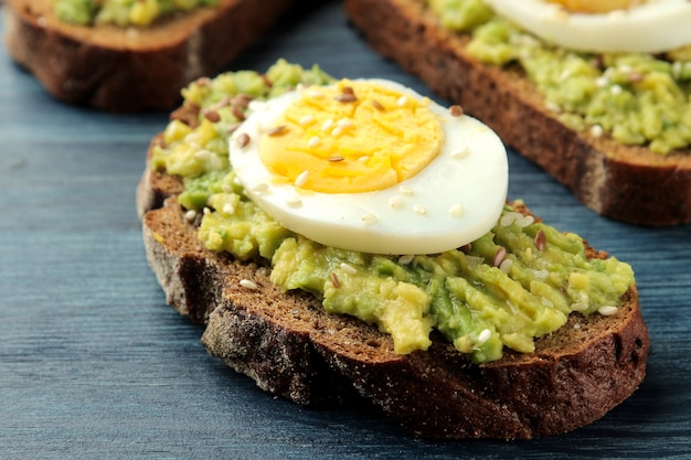 Sandwich avec purée d'avocat et oeuf sur une table en bois bleu close-up