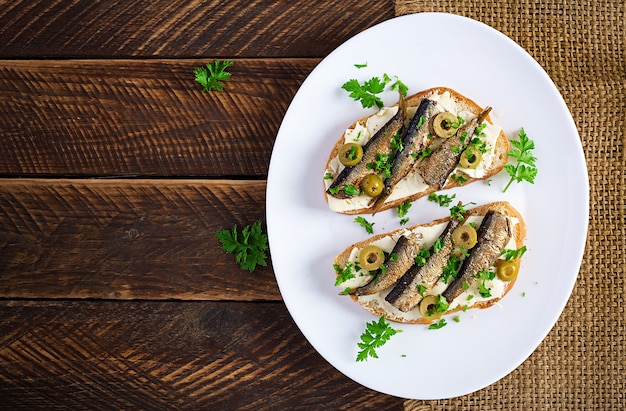 Sandwich - smorrebrod avec sprats, olives vertes et beurre sur table en bois. Cuisine danoise. Vue de dessus, frais généraux, pose à plat