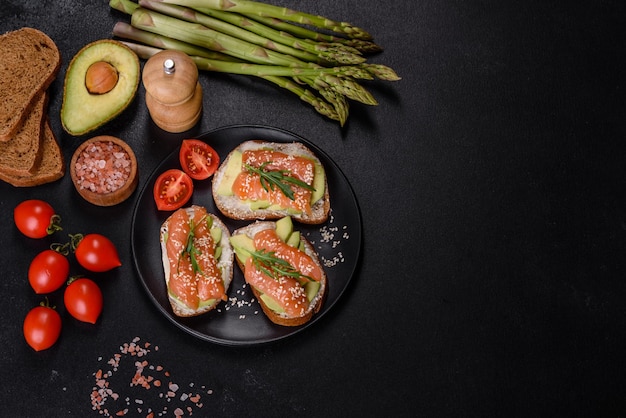 Sandwich toast au beurre d'avocat et de saumon décoré de roquette et de graines de sésame sur fond de pierre noire