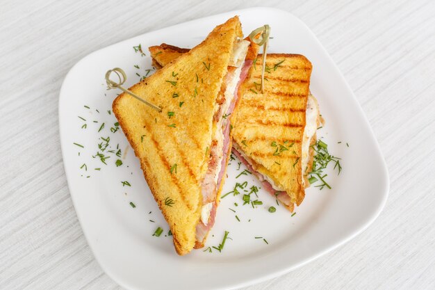 Sandwich toast grillé au fromage, bacon et salade sur table en bois blanc, surface