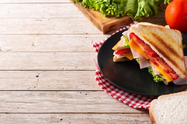 Sandwich à la tomate, laitue, jambon et fromage sur table en bois