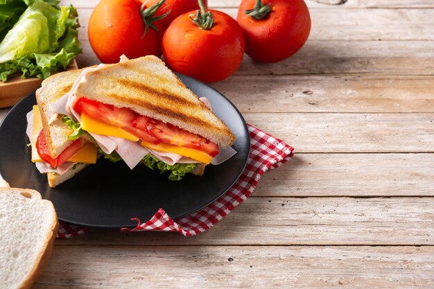 Sandwich à la tomate, laitue, jambon et fromage sur table en bois