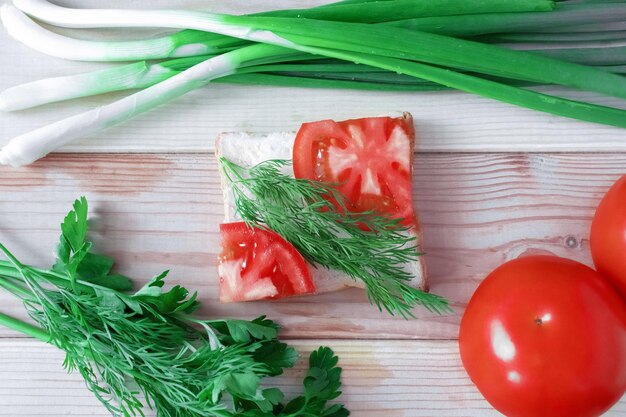 Sandwich avec des tomates et des herbes sur un fond en bois en gros plan