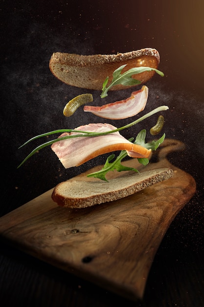 Un sandwich avec une tranche de bacon et des ingrédients volants